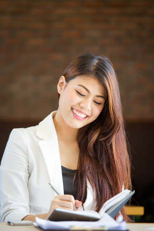 Beautiful Asian women writing on her notebook in the coffee shop close up.の写真素材