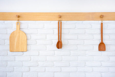 Wooden kitchen tools hanging on the bricks wall close up.