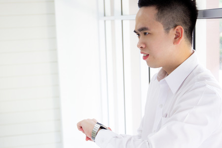 Portrait of upset smart Asian man looking at a watch close up.