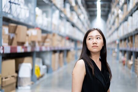 Beautiful Asian woman's portrait in warehouse.  Asian woman looking for the items on shelf close up.の写真素材