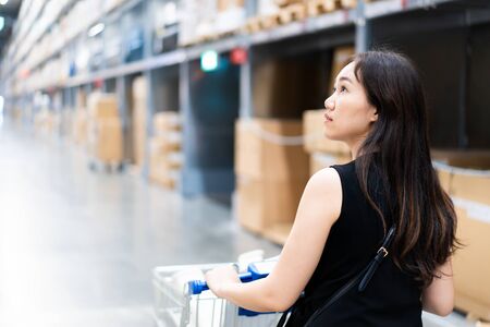 Beautiful Asian woman's portrait in warehouse.  Asian woman looking for the items on shelf close up.の写真素材