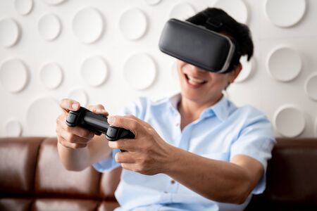 Asian adult man playing video game by using Virtual Reality goggle (VR) in the living room....