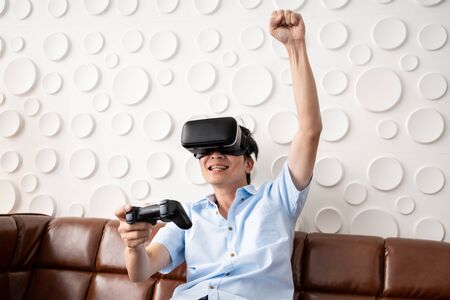 Asian adult man playing video game by using Virtual Reality goggle (VR) in the living room....