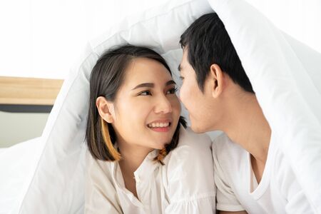 Asian young couple talking together on the bed in morning, concept of relationship between man and woman in everyday life.の写真素材
