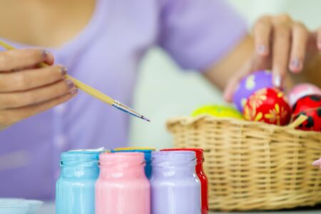 Asian young pretty woman enjoy painting a water colors on fantasy eggs for Easter egg festival. Beautiful colorful fancy Easter egg in bucket. The symbolic of Easter egg festival concept.の写真素材