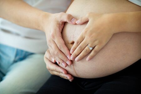 Asian lovely husband and wife portrait, his wife is in pregnancy. Husband tenderly hug and kiss his...