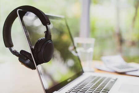 Businessman hanging his modern wireless headphones over the laptop computer screen while taking a break. Setting up working space or home office. Work from home concept with copy space for background.の写真素材