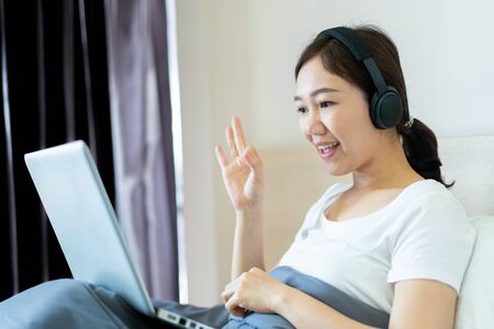 Asian young woman's portrait in working at home concept. Happy Asian woman showing OK sign during using video conference with her friend during stay at home. Joyful woman browsing the internet.の写真素材