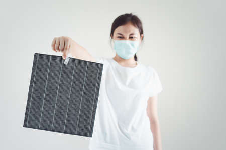 Asian woman wearing a hygiene protective face mask during changing a dirty air filter in the air purifier machine close up with copyspace. Hygienic lifestyle and prevention from illness concept.の写真素材