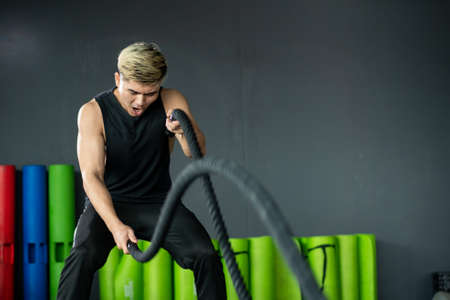 Strong Asian sportive man standing in a ready position for doing a battle rope exercise in a indoor...