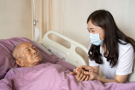 Asian people family, granddaughter visiting her grandfather at hospital. Very old Asian man got a sickness and health problem. Woman with face mask taking care her grandfather.の写真素材