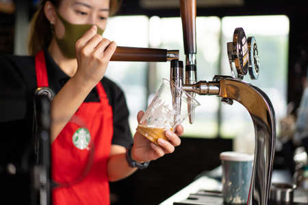 Nonthaburi - Thailand November 22, 2020: Professional Starbucks's barista pouring a Nitro Cold Brew coffee from the Nitro Cold Brew machine tap into a Starbucks plastic cup close up.のeditorial素材