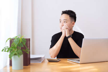 Asian young businessman in black shirt sitting in the relax working area and looking outside the...