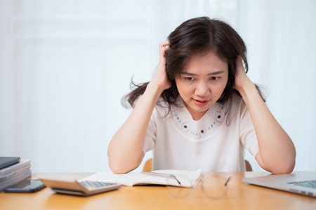 Asian woman feels upset and uncomfortable during working with a lot of document and overworking. Stressful and upset Asian young businesswoman catching at her head, woman worried about working problemの写真素材