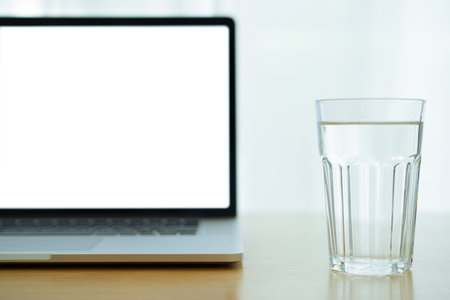 Notebook computer and drinking water in a glass on the wooden table in home office, purity drinking...