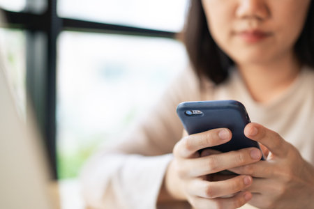Unrecognizable cheerful young businesswoman reading a message on a smartphone close up. Asian girl...