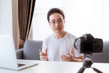 Asian video blog person or VLOG is now live streaming online through laptop and video camera, social...