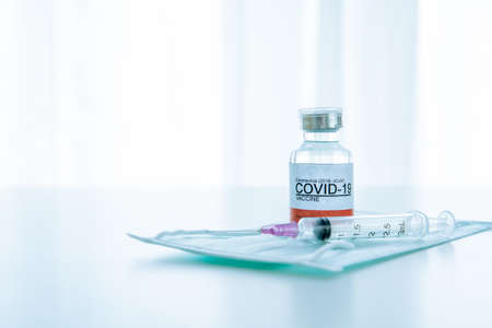 vaccine in a bottle with syringe and hygiene protective face mask on the table prepared for vaccinating. COVID19 Vaccine researching and development concept.の写真素材