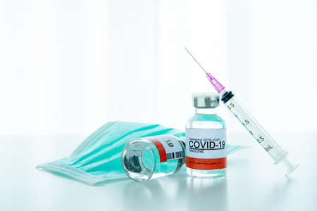 vaccine in a bottle with syringe and hygiene protective face mask on the table prepared for...