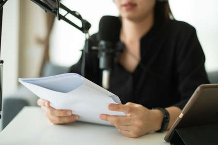 Happy Asian woman setting up a living room in her house for podcast studio, woman arranging a podcast and online radio station at home. Professional young podcaster speaking through a microphone.の写真素材