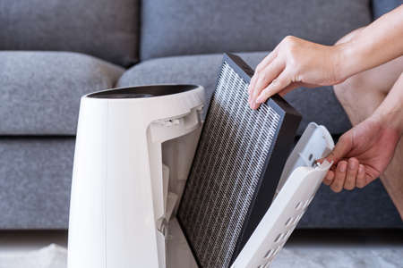 Unrecognizable Asian young man changing - fixing a dirty air purifier HEPA filter after using for a...