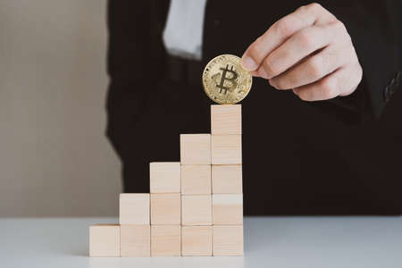 Unrecognizable businessman holding a physical Golden Bitcoin - BTC on the top of wooden block showing the growth of digital asset investment. Bitcoin and cryptocurrency asset investment concept.の写真素材