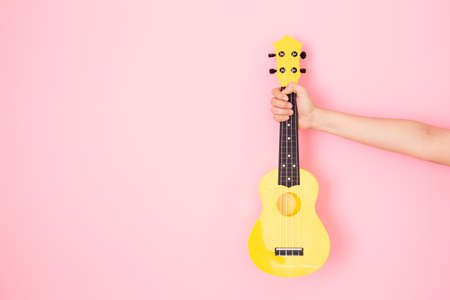 Happy Asian woman holds acoustic Ukulele guitar on pastel color background close up with copyspace. Cheerful young girl playing and practicing a Hawaiian guitar. Female hand holding the Ukulele.の写真素材