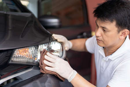 Asian man using a soft microfibre wiping and cleaning car exterior at the headlight close up. Car...