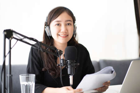 Beautiful and good looking young Asian woman arranging home podcast channel. Businesswoman recording her podcast for her online podcast live on the laptop computer and tablet. Modern working lifestyleの写真素材