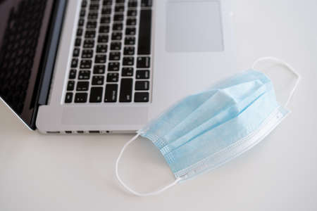 Hygiene protective face mask and laptop computer on the table in home office close up with copyspace. Healthcare and new normal concept in 2019 pandemic.の写真素材
