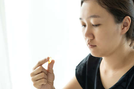 Beautiful young Asian woman holding a fish oil capsule on her hand close up. Nutrition and vitamin supplements product. Soft Gell pill on woman's hand.の写真素材