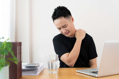 Asian young man having a heath problem from working with out relaxing, office syndrome problem. Stressful workaholic Asian businessman feels backache and headache - shoulder pain.の写真素材
