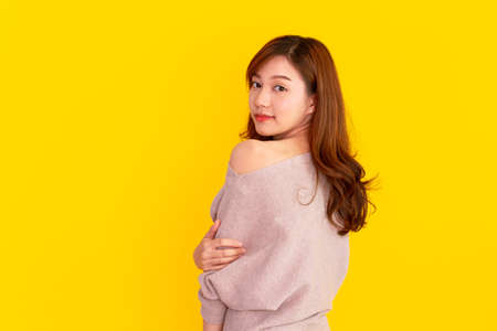 Beautiful Asian young woman's portrait on bright yellow background, Studio portrait of Asian girl showing her beautiful shoulder and smile to camera with copyspace. Pretty Asia girl  happy posing.の写真素材