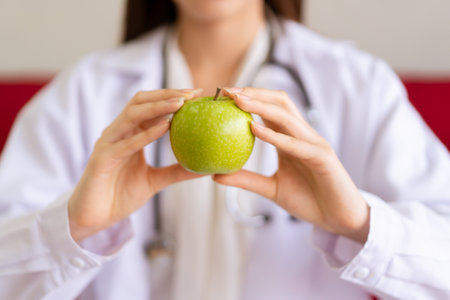 Unrecognizable Asian expert nutritionist showing an organic green apple close up, nutrition consultant portrait. Healthcare and healthy eating for healthy people concept.の写真素材