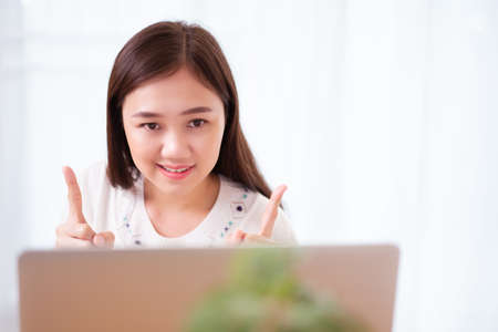 Happy Asian young woman working at home, working from home is the new working solution during the COVID-19 pandemic and able to increase working productivity. Asian beautiful girl using video call.の写真素材