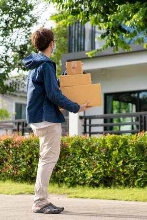 Asian postman with a hygiene protective face mask picking up a parcel package or parcel box from the truck for deliver to customer's door. New Normal concept during covid-19 or coronavirus pandemicの写真素材