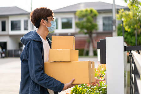 Asian postman with a hygiene protective face mask picking up a parcel package or parcel box from the...
