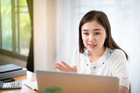 Happy Asian young woman working at home, working from home is the new working solution during the COVID-19 pandemic and able to increase working productivity. Asian beautiful girl using video call.の写真素材