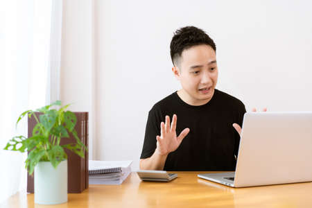 Happy Asian young businessman in relax casual style doing a video conference with his colleague, using online meeting and video conference for avoiding COVID-19 pandemic. New normal lifestyles.の写真素材
