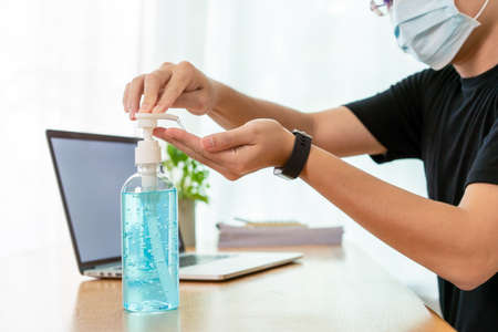 Unrecognizable Asian man with hygiene protective face mask is pumping a liquid hand sanitizer from a bottle close up. COVID-19 or Coronavirus pandemic awareness in everyday life, the new normal.の写真素材