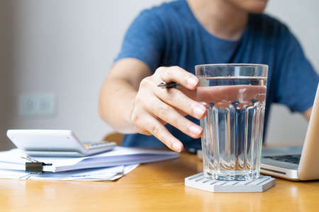 Businessman in relaxing casual working from home. Modern working lifestyle concept with copy space. Man drinking a mineral water in glass during working, refreshment during hard working.の写真素材