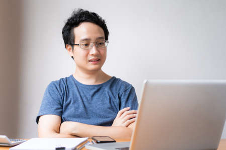 Young Asian businessman in relax casual during working from home. Asian man staying at home and setup a small workplace during COVID-19 self isolation. Work from home concept during coronavirus crisisの写真素材