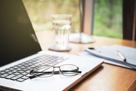 Eyeglasses on laptop computer keyboard close up with copyspace. Work from home concept. Workspace corner at home with laptop computer, notebook, paper, eyeglasses and drinking water glass close up.の写真素材