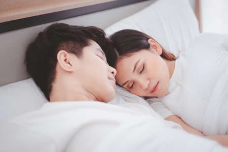 Lovely husband and wife sleeping together on the bed in bedroom close up. Husband embracing his...