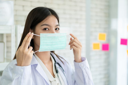 Asian woman doctor masking on a hygiene protective face mask while working in the hospital. Health care staff working in the pandemic or outbreak area of COVID-19. Coronavirus outbreak concept.の写真素材