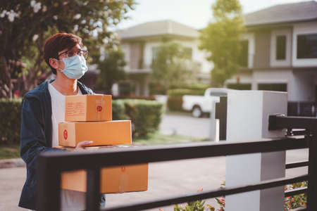 Asian postman with a hygiene protective face mask picking up a parcel package or parcel box from the truck for deliver to customer's door. New Normal concept during covid-19 or coronavirus pandemic.の写真素材