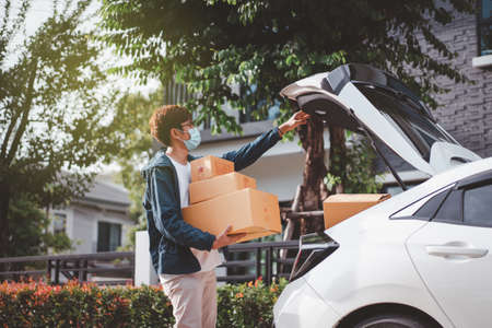 Asian postman with a hygiene protective face mask picking up a parcel package or parcel box from the truck for deliver to customer's door. New Normal concept during covid-19 or coronavirus pandemic.の写真素材