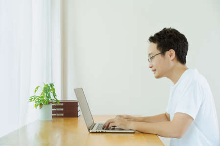 Happy Asian young businessman in relax casual style doing a video conference with his colleague, using online meeting and video conference for avoiding COVID-19 pandemic. New normal lifestyles.の写真素材