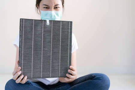 Asian woman wearing a hygiene protective face mask during changing a dirty air filter in the air purifier machine close up with copyspace. Hygienic lifestyle and prevention from illness concept.の写真素材