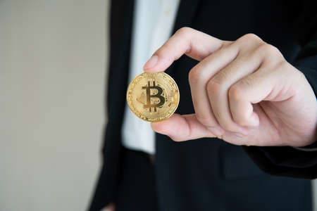 Unrecognizable businessman holding and showing a golden physical Bitcoin or BTC to camera with...